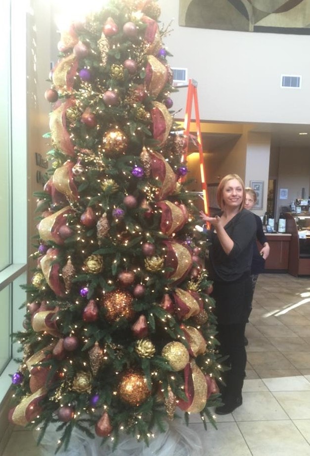 Tall Christmas tree with burgundy, gold and purple ornaments in commercial lobby with Megan posing beside it