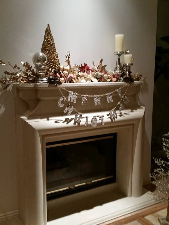 Fireplace mantel with gold Merry Christmas banner, gold bottle brush tree, deer figurine and candles
