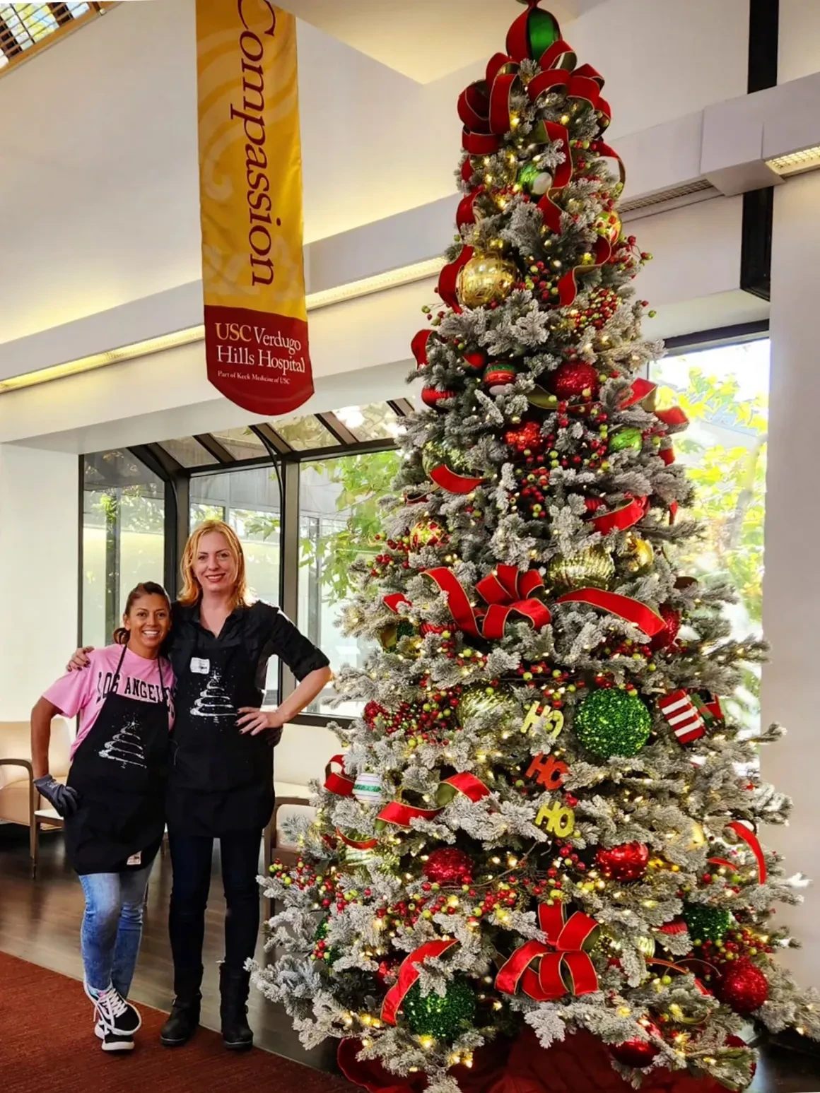 Two women posing beside decorated Christmas tree