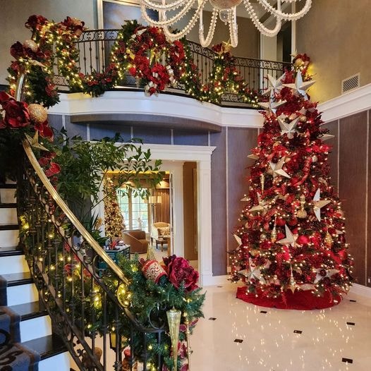 Grand staircase with red and gold Christmas garland and large decorated tree in foyer